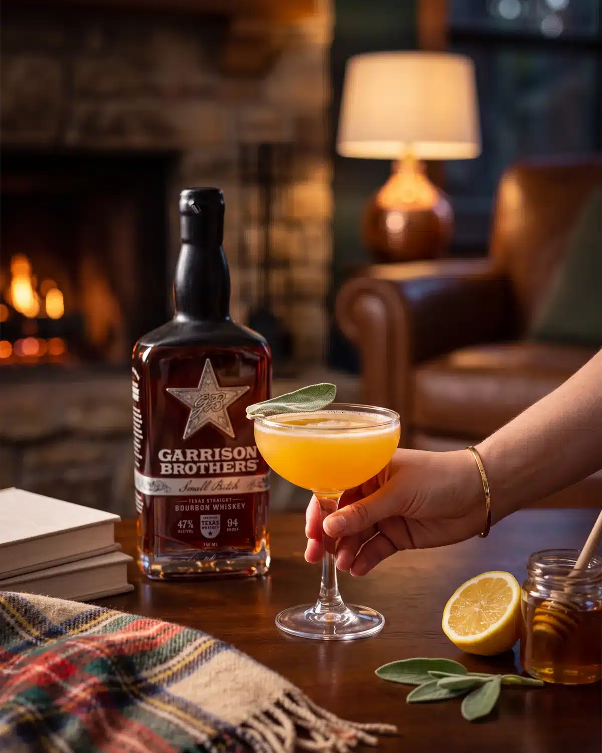 Bee's Knees bourbon cocktail by a stone fireplace with a bottle of Garrison Brothers Small Batch Bourbon