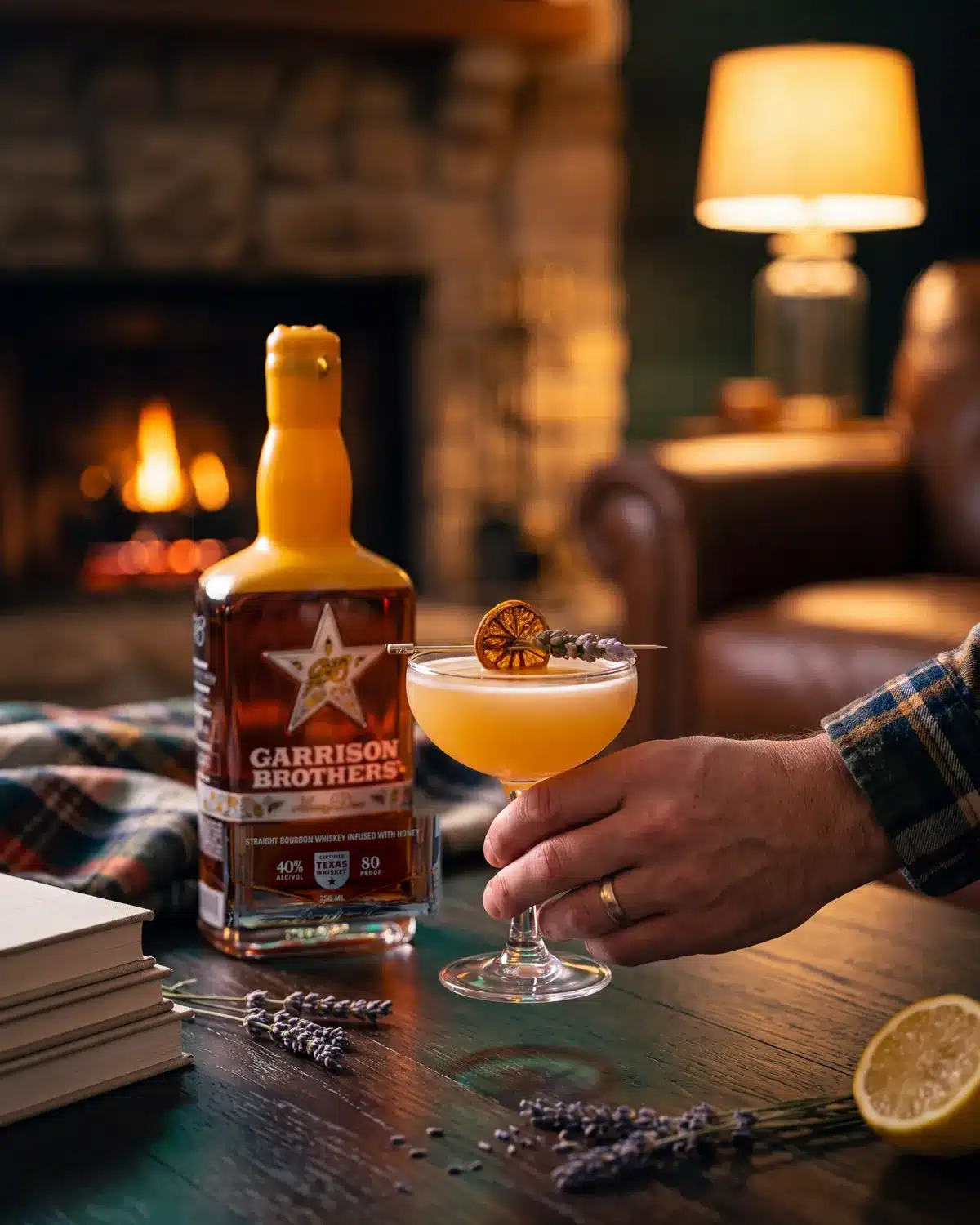 Busy Little Bees bourbon cocktail by a stone fireplace with a bottle of Garrison Brothers HoneyDew Bourbon