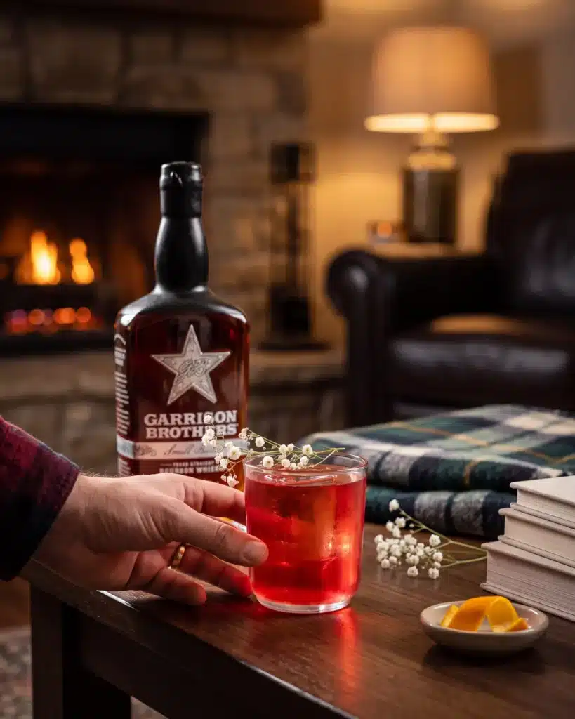 Old Fashioned Sloe-Cookin' bourbon cocktail by a stone fireplace with a bottle of Garrison Brothers Small Batch Bourbon