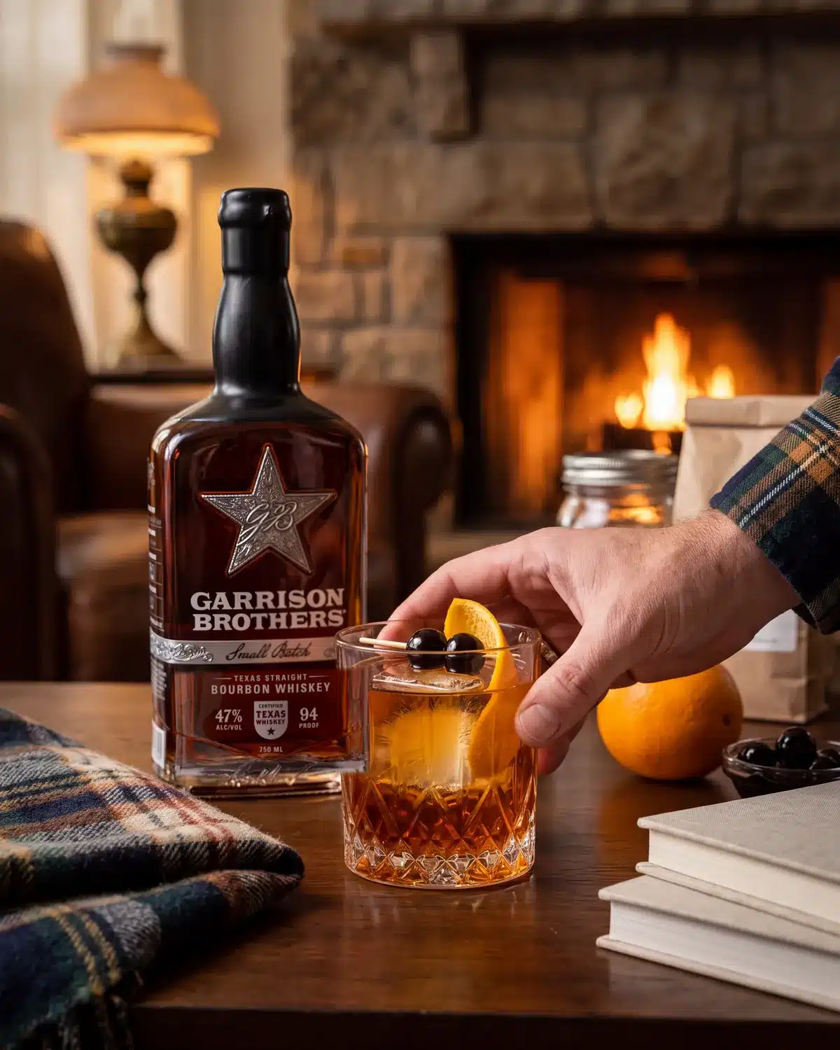 Classic Old Fashioned bourbon cocktail by a stone fireplace with a bottle of Garrison Brothers Small Batch Bourbon