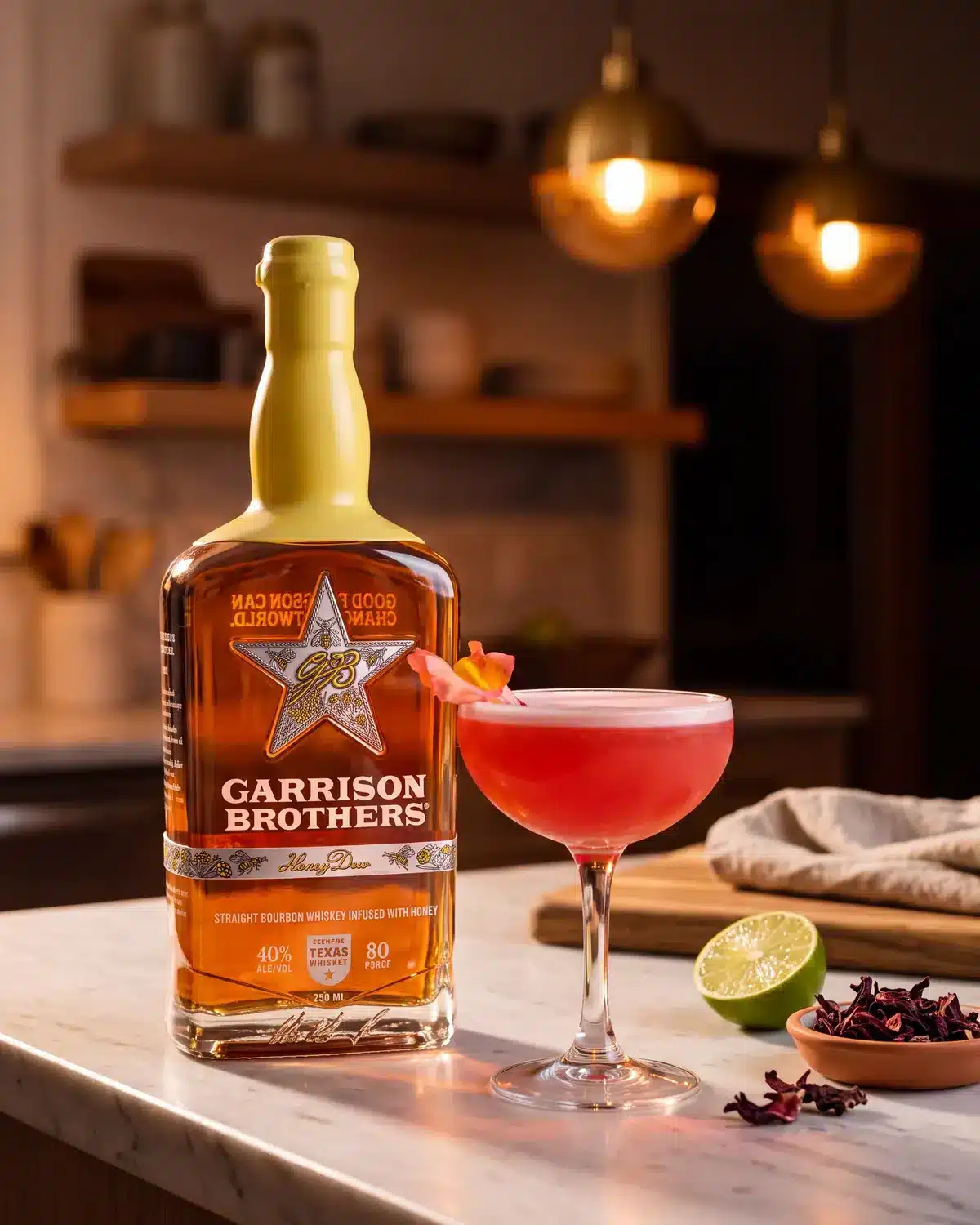 Honey Hye-Biscus bourbon cocktail on a kitchen counter with a bottle of Garrison Brothers HoneyDew Bourbon