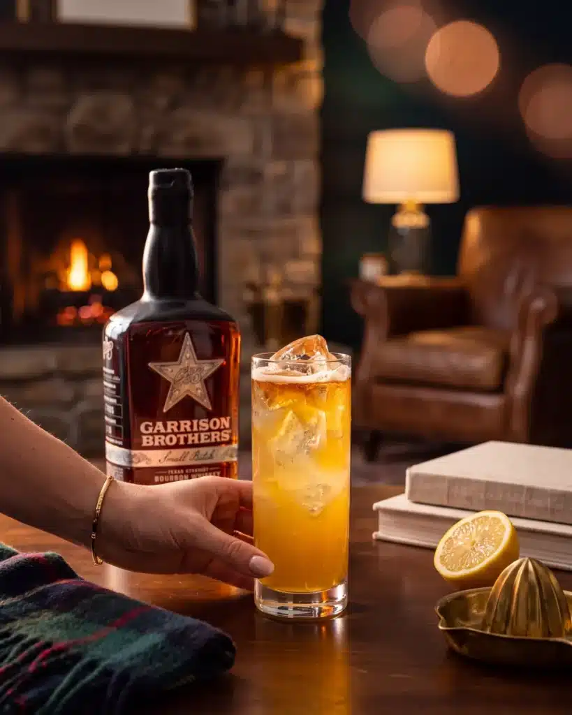 The Rattlesnake bourbon cocktail by a stone fireplace with a bottle of Garrison Brothers Small Batch Bourbon