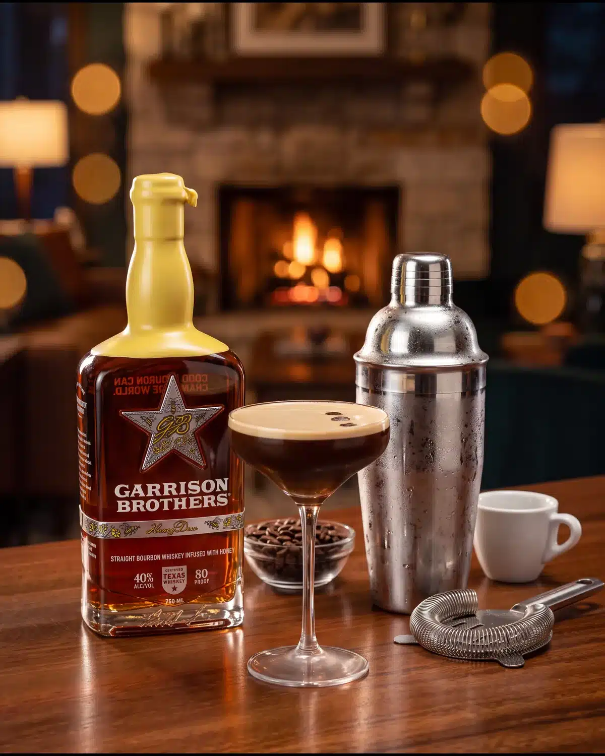 Midnight Drifter bourbon cocktail by a stone fireplace with a bottle of Garrison Brothers HoneyDew Bourbon