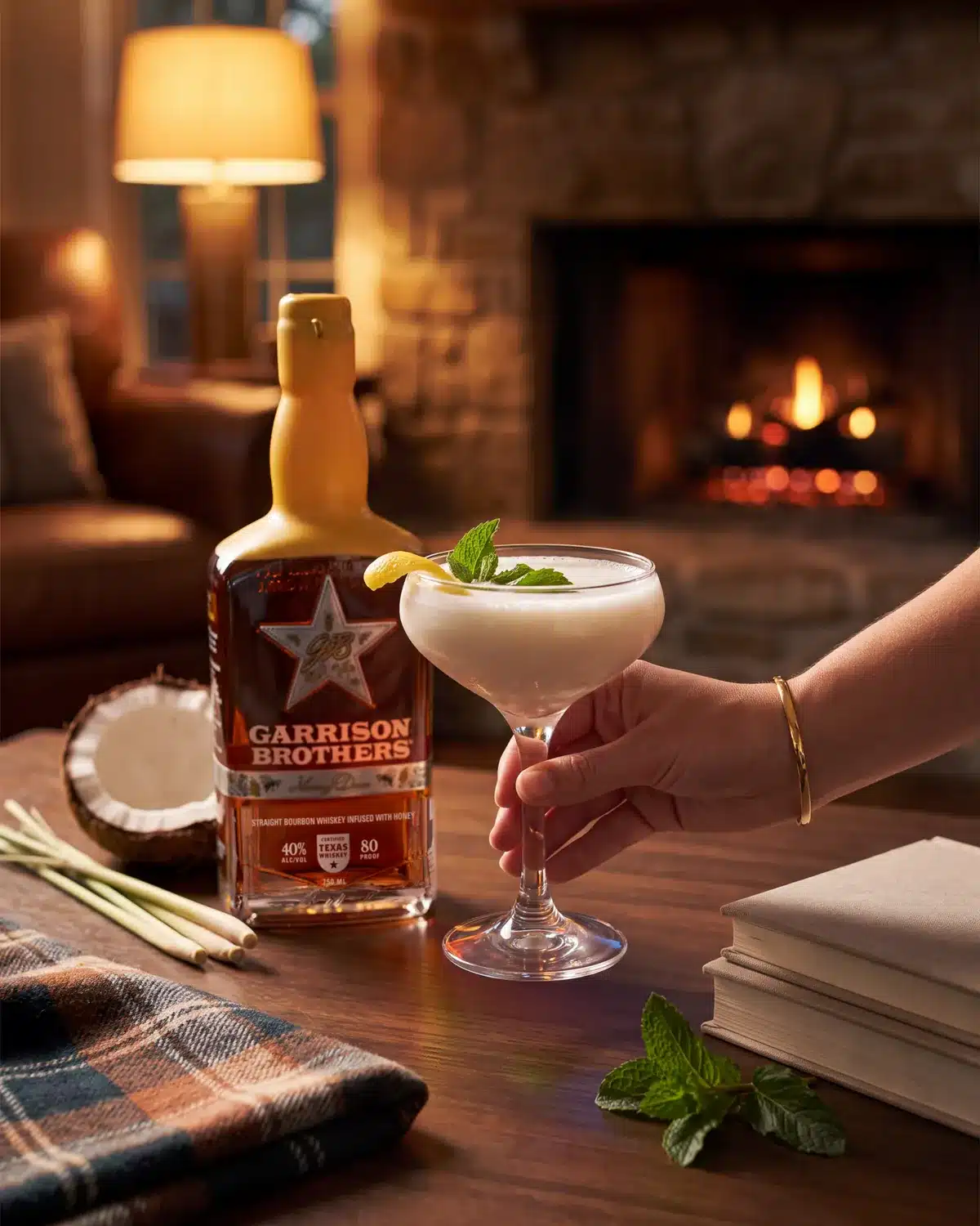 Coco Spice bourbon cocktail by a stone fireplace with a bottle of Garrison Brothers HoneyDew Bourbon