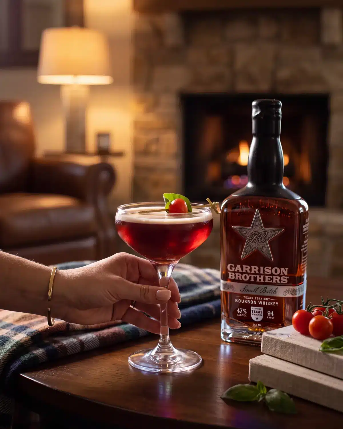 Rojo Fresco bourbon cocktail by a stone fireplace with a bottle of Garrison Brothers Small Batch Bourbon